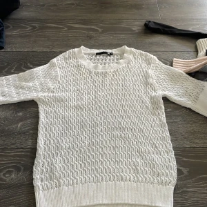 Vit stickad tröja från 157 XS - Säljer en vit stickad tröja från 157 i storlek XS. Tröjan har ett snyggt hålmönster över hela och ribbade muddar vid hals, ärmslut och nederkant. Modellen har trekvartsärm och är perfekt för dig som gillar en fräsch och clean look.