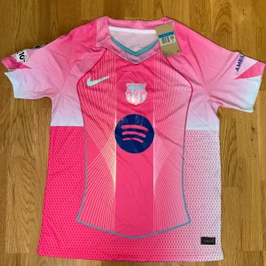 Barça x Nike rosa fotbollströja med champion league  - Snygg FC Barcelona x Nike fotbollströja i olika rosa nyanser med vita och blå detaljer. Kortärmad med coolt grafiskt mönster och tryck från Spotify, Ambilight tv och UEFA Foundation på ärmen. Och champions league 