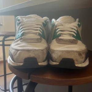 Nike Air Max 90 vit/grön sneakers - Nike Air Max 90 sneakers med vit mesh och skinn, gröna och svarta detaljer samt klassisk Air Max-sula. Snygg retrostil med rund tå och platt sula, vita snören och tydlig Air Max-logga på sidan och bak. Perfekt för dig som gillar streetwear och sportig vibe. De är använda så finns lite slitningar. Priset går att diskutera