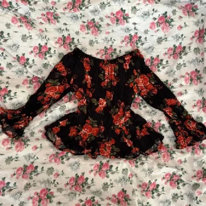 Blommig offshoulder blus - Supersöt svart offshoulder blus med röd/orangea blommor från H&M i strl 32. Utsvängda ärmar samt volang vid midjan och ärmslut. Perfekt för dig som gillar romantisk och boho stil!💞