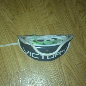 Svart Unihoc glasögon - Säljer ett svart och vitt glasögonfodral från Unihoc med halvmåneformad design och tydlig logga. Fodralet är gjort i slitstark polyester och har dragkedja samt snörning. Perfekt för att skydda sportglasögon när du är på språng.