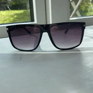 Ray bad boyfriend  - Snygga svarta solglasögon med breda bågar och fyrkantig form. Glasen är tonade i mörkgrått och bågarna har små silvriga nitar vid hörnen för extra detalj. Perfekt accessoar för att höja din stil på sommaren. Nästan exakt lika som ray bans.