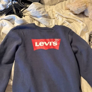 Mörkblå Levi's sweatshirt med logga - Säljer en mörkblå sweatshirt från Levi's med den klassiska röda loggan tryckt på bröstet. Tröjan har rund hals, långa ärmar och är gjord i mjuk bomullsmix som är skön mot huden. Perfekt för dig som gillar streetwear och vill ha en enkel men snygg look.