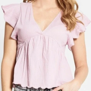 Ljusrosa blus med volangärmar - Supersöt ljusrosa blus med v-ringning och volangärmar. Toppen har en luftig passform, knytning i ryggen och vågig kant nedtill. Perfekt för dig som gillar romantiska detaljer och en chill vibe. Materialet känns lätt och skönt mot huden.