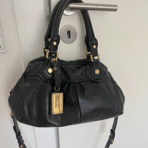 Svart handväska från Marc Jacobs - Snygg svart handväska från Marc Jacobs med guldfärgade detaljer och logoplatta framtill. Längd:33 bredd:15 höjd:17