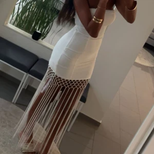 Vit långklänning med fransdetaljer - Säljer en vit långklänning med axelbandslös design och slim passform. Använd en gång endast