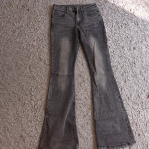 Grå bootcut jeans (ljusare färg än på bild) - Säljer ett par grå jeans med snyggt tvättad look och bootcut-ben. Klassisk femficksmodell med dragkedja och knapp framtill. Jeansen har breda ben och är tillverkade i jeansmaterial med lite stretch. Perfekt för dig som gillar retrostil och vill sticka ut. Tyvärr har jag råkat trampa sönder de bakifrån men om man är kort är det bara att sy in eller så kan man ha dem så☺️
