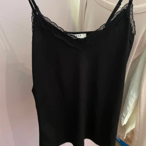 Svart linnetopp med spets från Pieces - Svart linnetopp från Pieces med tunna axelband och snygg spetskant vid halsringningen.