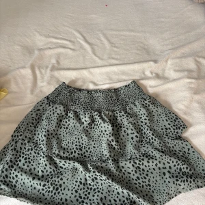 Leopardmönstrad grön kjol från ONLY XS - Supersöt kort kjol från ONLY i ljusgrönt med svart leopardmönster. Kjolen har smock i midjan för en bekväm passform och volangig nederdel som ger en flowy känsla. Perfekt för dig som gillar trendiga prints och vill sticka ut lite extra.