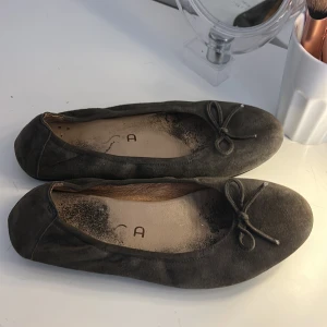Gråa ballerinaskor från Unisa - Snygga gråa ballerinaskor från Unisa i mjuk mocka med rund tå och en söt rosett framtill. Ballerina skorna är använda och ser värre ut än vad dom e !!!!!!❤️ går att byta sula! Skorna har platt sula och är perfekta för dig som gillar enkel och klassisk stil. Passar dig som vill ha bekväma och stilrena skor till vardags. Värda runt 1000kr 