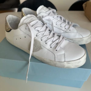 Philippe Model vita sneakers strl 40 - Snygga vita sneakers från Philippe Model med glittrig silverdetalj på hälen och en broderad patch på sidan. Skorna har rund tå, snörning och är tillverkade i skinn med gummisula. Perfekt för dig som gillar stilrena och trendiga sneakers med en twist. Skriv om ni har frågor eller om ni vill ha bättre bilder för de fick bara plats med 5 bilder😁 pris kan diskuteras. Kvitto medföljer om man vill.