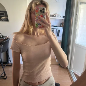 Offshoulder topp från Gina Tricot - Gammelrosa ribbad offshoulder topp från Gina Tricot. Toppen har volangdetaljer längs halsringningen och ärmen samt en croppad passform. Tillverkad i bomull från The Good Project-kollektionen. Jättefint skick!