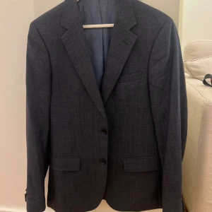 Mörkgrå kavaj från Bruun & Stengade - Snygg mörkgrå kavaj från Bruun & Stengade med klassisk passform. Kavajen har två knappar framtill, tre fickor. I storlek 48