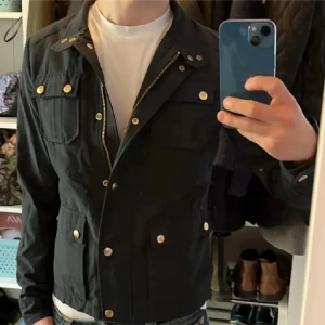 Marinblå woolrich jacka med unik design  - Säljer en marinblå jacka från Woolrich med snygga guldknappar och dragkedja. Jackan har fyra fickor framtill och en klassisk krage. Perfekt för dig som vill ha en stilren och tidlös look. Storlek S med sitter som XS 