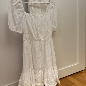 Vit broderad klänning från & Other Stories - Superfin vit klänning från & Other Stories med broderade detaljer och puffärmar. Klänningen har en volang nertill och knytband i ryggen. Perfekt för sommarens alla tillfällen!
