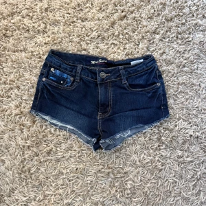 Mörkblå Jeansshorts   från Miss Swan - Snygga mörkblå jeansshorts från Miss Swan i storlek 38, lågmidja med glitter detaljer på fickorna.
