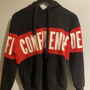 Confidence hoodie - En svart röd hoodie med texten ”confidence” tvärs över. Använt men bra skick.🎀