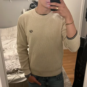Beige stickad tröja från Fred Perry - Säljer en beige stickad tröja från Fred Perry med svart broderad logga på bröstet. Tröjan är knappt använd och har inga defekter. Pris kan diskuteras. Tveka inte att skriva om ni undrar det minsta!