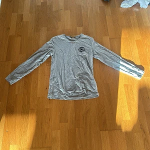Grå långärmad tröja från Burberry - Säljer en stilren grå långärmad tröja från Burberry. Tröjan har rund halsringning och en liten logga på bröstet. Perfekt för dig som gillar klassiska och enkla plagg med exklusiv känsla.