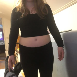 Svart croppad långärmad topp - Säljer en svart croppad topp med långa ärmar och rund halsringning. Toppen är ribbad och har en tight passform, perfekt att styla med höga jeans eller kjol. Enkel och stilren design som passar till många tillfällen.