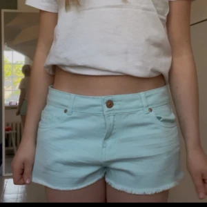 Turkosa/blå shorts - Säljer ett par lågmidjade ljusblå/turkosa jeansshorts. Bra skick. Perfekta till sommaren. 42 i midjemått, 88 runt om hela