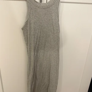Grå ribbad långklänning från 157 - Säljer en enkel och stilren grå ribbad midklänning från 157. Klänningen är ärmlös och har en rund halsringning. Tillverkad i mjuk bomullsblandning med viskos för extra komfort. Perfekt för en avslappnad look. Går till knäna på mig, 170cm