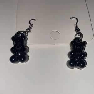 Svarta gummibjörns örhängen INGA PLUPPAR - Unika örhängen med gummibojörnar. Hängande modell med metallkrok. Perfekta för att ge en cool touch till din outfit.