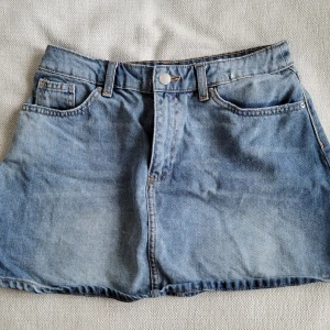 Blå kort jeanskjol  - Säljer en blå jeanskjol i klassisk modell med fem fickor, bälteshällor och dragkedja framtill. Kjolen är kort och har en rak passform som ger en avslappnad vibe. Perfekt att styla med en crop top eller hoodie. Jag är 173cm för referens, tyckte den var lite kort på mig därför jag säljer vidare🤗