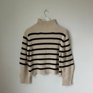 Randig stickad polotröja från Carin Wester - Säljer en beige och svart randig stickad polotröja från Carin Wester i storlek XS. Tröjan har lång ärm, hög polokrage och är ribbstickad. Materialet är 60% bomull och 40% akryl. Perfekt för kyligare dagar! Artnr: Ö295