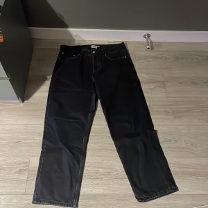 Svarta jeansbyxor från 157 - Säljer ett par svarta jeansbyxor från 157 med klassisk femficksdesign och raka ben. Byxorna har baggy passform och stängs med dragkedja och knapp. Perfekta för dig som diggar streetwear! Skick 10/10 endast andvänt fåtal gånger. Storlek 32/32