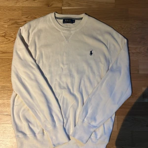 Vit tröja från Polo Ralph Lauren - Klassisk vit tröja från Polo Ralph Lauren med rund halsringning och broderad logga på bröstet. Tröjan har långa ärmar och ribbade muddar vid ärmslut och nederkant. Perfekt för en clean och stilren look.