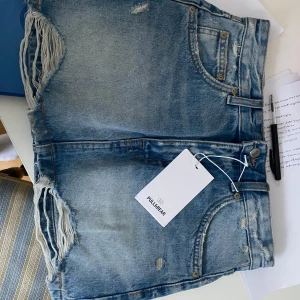 Blå jeansshorts från Pull&Bear - Säljer ett par blå jeansshorts från Pull&Bear i storlek S. Shortsen har slitna detaljer och fransar vid benen, klassisk femficksmodell och knappgylf. Perfekta för sommaren och ger en avslappnad look.