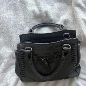 Grå handväska med snygga detaljer💕❤️ - Säljer en grå jättesnygg handväska med snygga flätade detaljer på sidorna och praktiska fack. Väskan har både handtag och avtagbar axelreml. Perfekt för dig som vill ha en stilren och rymlig accessoar. Skriv vid frågor💕💕