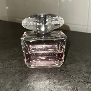 Versace Bright Crystal Eau de Toilette 100ml kvar - Versace Bright Crystal är en lyxig parfym i en elegant, fyrkantig glasflaska med ljusrosa doftvätska. Flaskan har en stor, kristalliknande transparent kork som ger exklusiv känsla. Perfekt för dig som gillar fräscha och blommiga dofter. 200 ml men halva kvar, så ca 100 ml. Är inte tung utan väldigt fräsch och ungdomlig! Pris kan diskuteras men tänk på att detta är 100ml Versace! 
