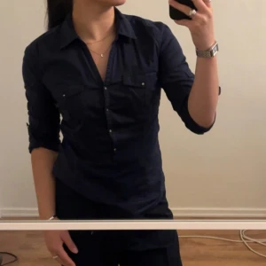 Marinblå skjorta - Marinblå skjorta, samma modell som ett tidigare inlägg. Storlek M, men passar även till S. Använd, men inte tecken på slitage. Fina knappdetaljer i silverfärg. Ärmarna är uppvikta, men kan vikas ut till en hel armlängd