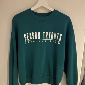 Mörkgrön sweatshirt från Gina Tricot - Säljer en Mörkgrön sweatshirt från Gina Tricot med trycket 'SEASON TRYOUTS JOIN THE TEAM' i vitt framtill. Tröjan har rund halsringning och långa ärmar. Perfekt för en avslappnad stil.