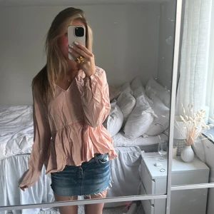 Ljusrosa blus med volang - Säljer en söt ljusrosa blus med v-ringning och volang nertill. Blusen har långa ärmar och är tillverkad i ett lätt material som passar perfekt till våren eller sommaren. Superfin att matcha med jeanskjol eller shorts!