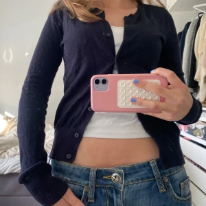 Mörkblå kofta från H&M - Säljer en enkel och klassisk mörkblå kofta från H&M Basic. Koftan har lång ärm, rund halsringning och knäppning framtill. Perfekt att slänga över en topp eller linne för en stilren look.