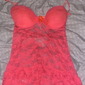 Rosa spetsig babydoll-linnetopp - Säljer en rosa babydoll-linnetopp i spets med vadderade kupor och liten rosett framtill. Tunt och genomskinligt material, perfekt för att känna sig extra fin. Justerbara axelband för bästa passform.