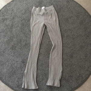 Beige ribbade byxor från Gina Tricot - Säljer ett par beige ribbade sköna mys byxor från Gina Tricot. Byxorna är utsvängda i benen, har ett litet slit längst nere på benen och är tillverkade i ett mjukt, stretchigt material. Perfekta för att bara gå om kring i hemma eller att sova i. Har en pytteliten fläck på ena benet men inget som märks särskilt mycket. 💕