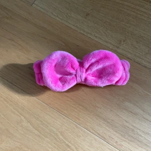 Rosa fluffig sminkdiadem med rosett från H&M - Supermjukt och fluffigt rosa sminkdiadem från H&M med en stor rosett framtill. Perfekt accessoar för att hålla håret borta vid sminkning eller hudvård. Diademet är elastiskt och täckt i ett syntetmaterial som känns skönt mot huden.