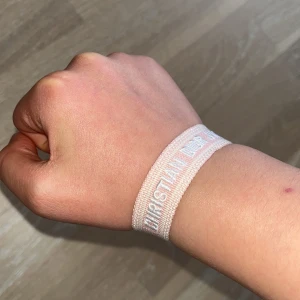 Rosa armband från Christian Dior - Säljer ett ljusrosa armband från Christian Dior med broderad logga i vitt. Armbandet har justerbar knytning med två tofsar i ändarna. Perfekt accessoar för att lyfta din outfit med en exklusiv touch.