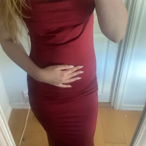 Vinröd långklänning med draperad överdel - Säljer en elegant vinröd långklänning med draperad överdel och figurnära passform. Klänningen är ärmlös och har en stilren, enkel design som framhäver siluetten. Perfekt för speciella tillfällen.