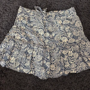 Blommig kortkjol med volang - Supersöt kortkjol med blommigt mönster i mörkblått och vitt. Kjolen har volang nertill, snörning i midjan och inbyggda shorts🫶