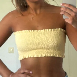 Gul tubtopp - Säljer en ljusgul bandeau tubtopp från Gina Tricot i storlek S. Toppen är smockad med volangkant upptill och nedtill