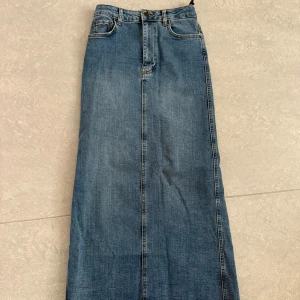 Lång jeanskjol med slits från Zara - Lång blå jeanskjol från Zara. Kjolen har en slits bak och en rak passform. Köpt secondhand, använd men i gott skick.