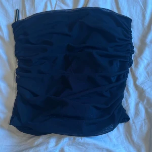 Svart meshlinne från Gina Tricot - Svart bandue topp från Gina Tricot i storlek S. Toppen är i mesh med snygga rynkade detaljer som ger en cool och trendig look. Perfekt att styla med en Kjol eller jeans för en modern vibe. Aldrig använd då den är för liten 