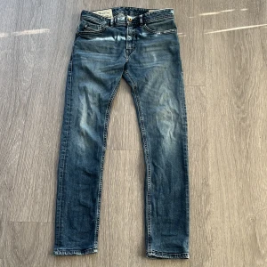 Blå slim jeans från Diesel - Snygga blå jeans från Diesel med klassisk femficksdesign och tydliga slitningar för en cool, använd look. Jeansen har skinny passform och är tillverkade i mjukt denim med detaljer som Diesel Industry-märke på myntfickan och svart patch bak i midjan.
