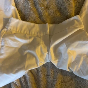 Vita vida kostymbyxor - Snygga vita kostymbyxor med låg midja och raka, vida ben. Byxorna har en stilren look utan synliga fickor eller detaljer och är sydda i ett slätt tyg som ger en clean känsla. Perfekta för dig som gillar minimalistisk och fräsch stil.