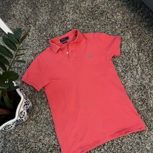 Rosa Polo Ralph Lauren pike - Snygg rosa t-shirt från Polo Ralph Lauren i slim fit med klassisk krage och korta ärmar. Ikoniska blå broderade loggan på bröstet. Tillverkad i mjuk bomull som är skön mot huden. Perfekt för dig som gillar stilren och sportig vibe.